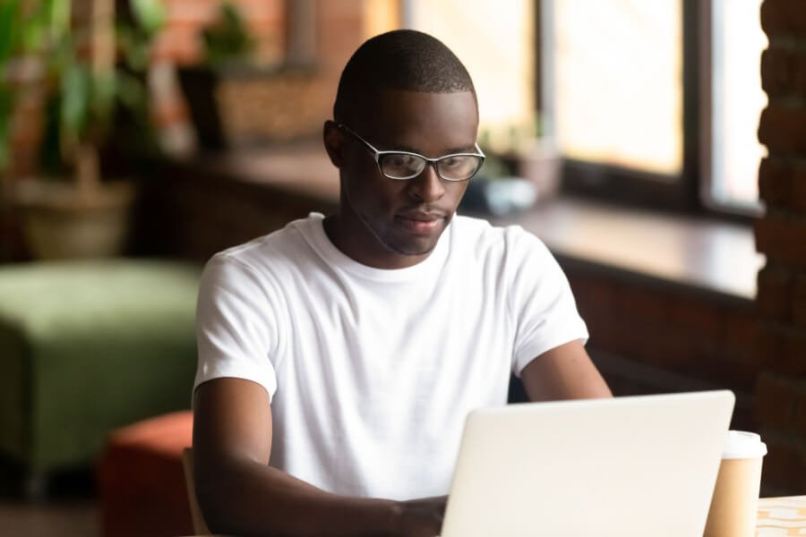Man sits in a café completing an online survey on his laptop