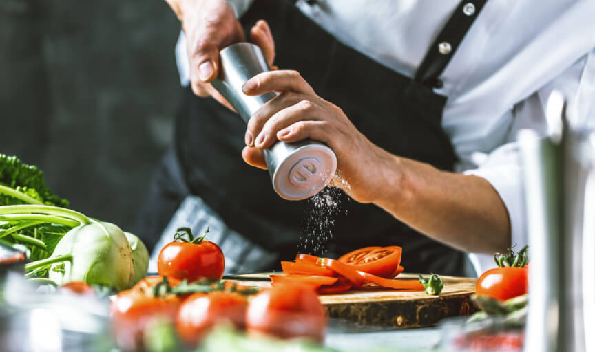 Chef adds seasoning to a salad in a restaurant.