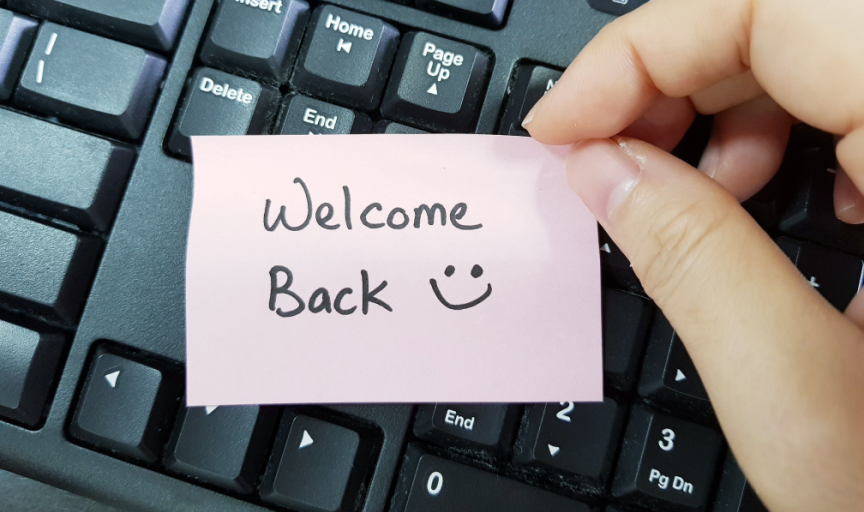 A returning employee's hand holds up a note reading "Welcome back"