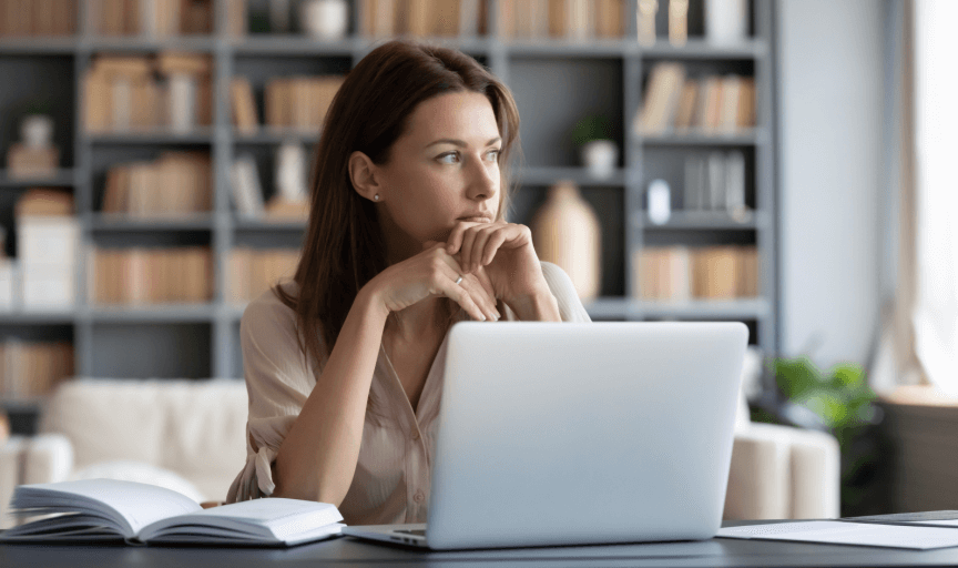 A young female employee sits at her laptop contemplating her response to an online survey measuring wellbeing