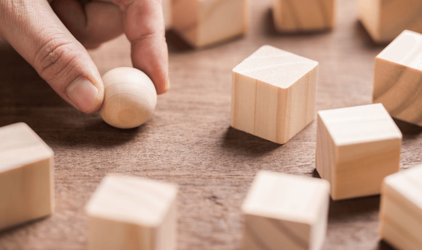 Closeup of a hand holding a round wooden sphere among an array of square wooden blocks, to illustrate the concept of brand metrics